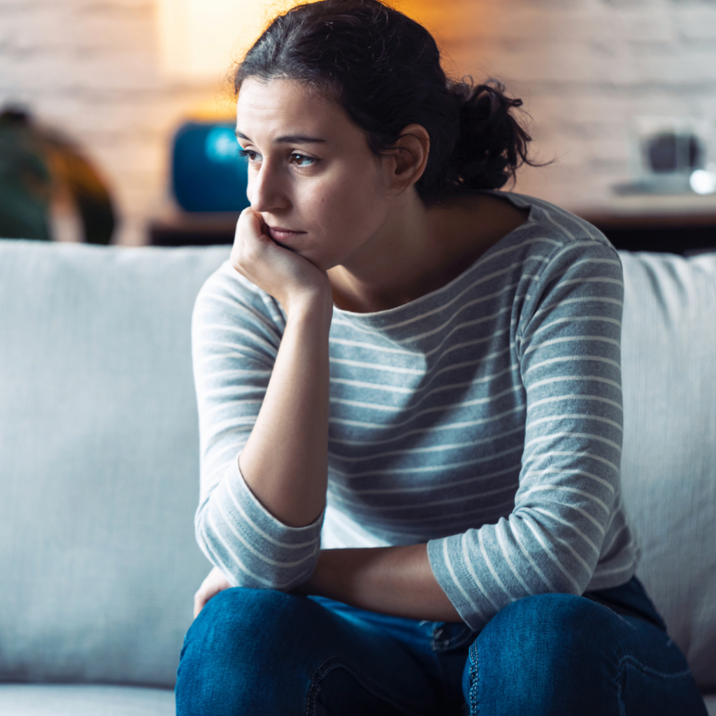 Woman sitting on a sofa looking pensive, reflecting emotional impact of baby loss on a partner