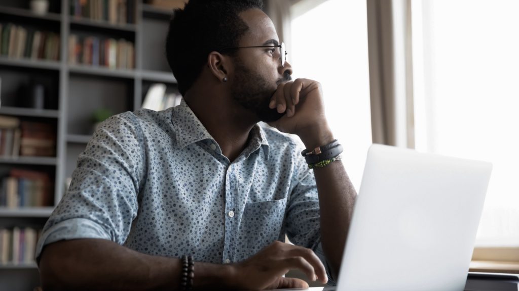 Man sitting at a desk with a laptop, trying to understand next steps and how to move forwards after miscarriage.