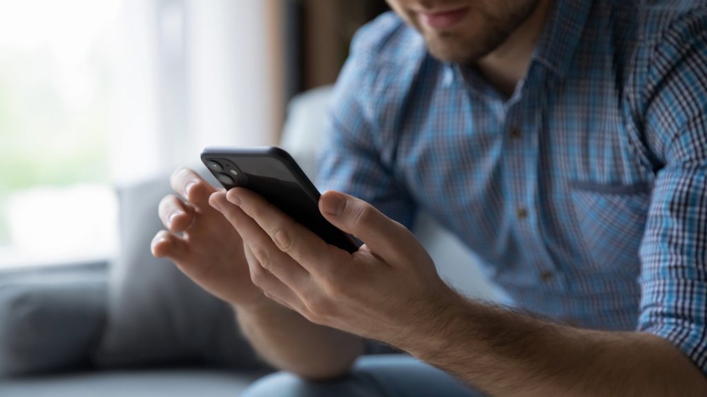Man sitting on a sofa using his phone to access Plan of Action information on miscarriage, taking action after loss.